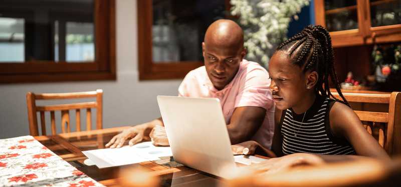 Adult instructs teen who's looking at laptop.