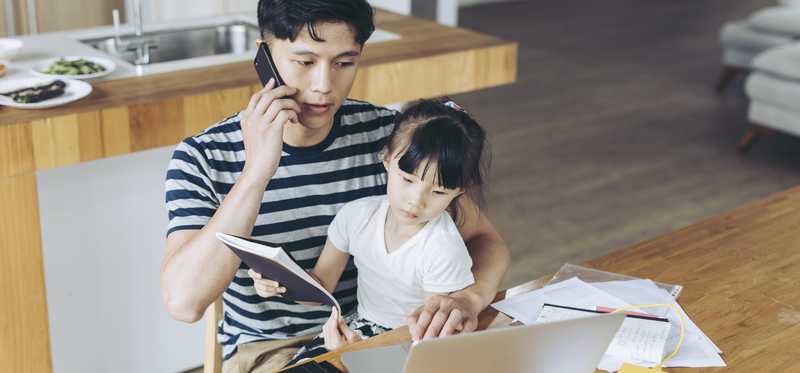 Person using laptop and phone with child on their lap.