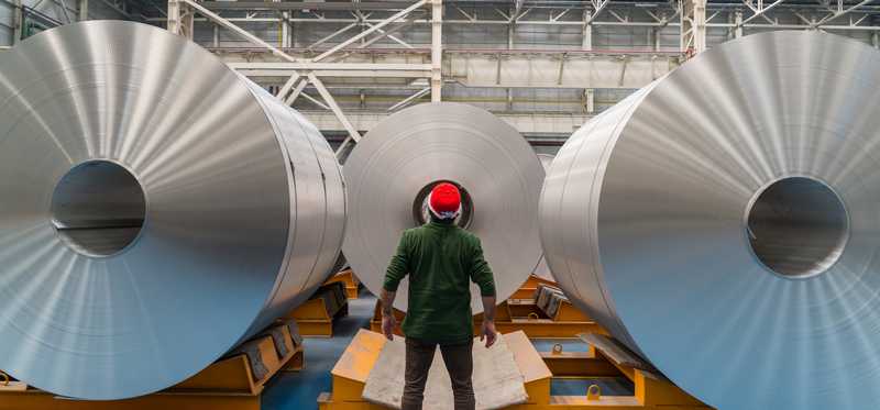 Person standing in front of large rolls of steel.