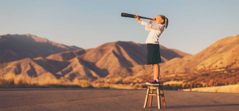 A person with a telescope is on a ladder in the desert.