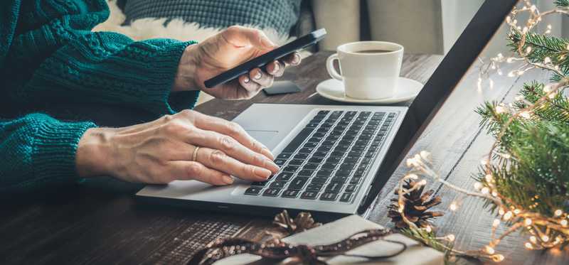 Person using smartphone and laptop at table decorated for the holidays