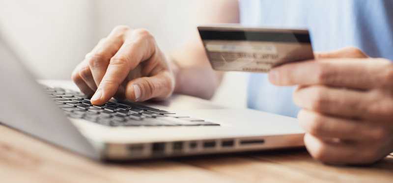 Person holding credit card and typing on laptop computer.