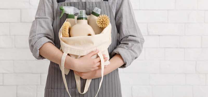 Person wearing apron and holding canvas bag filled with cleaning supplies