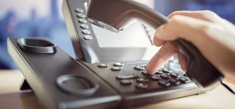 Person using a telephone on a desk.