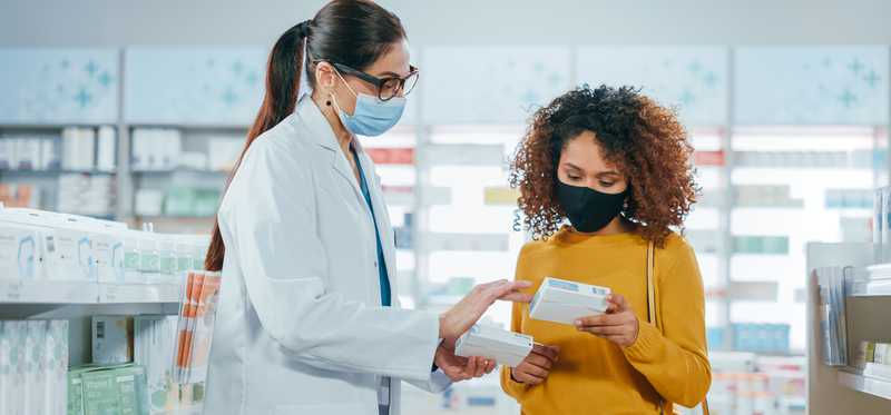 A pharmacist and a customer wearing masks.