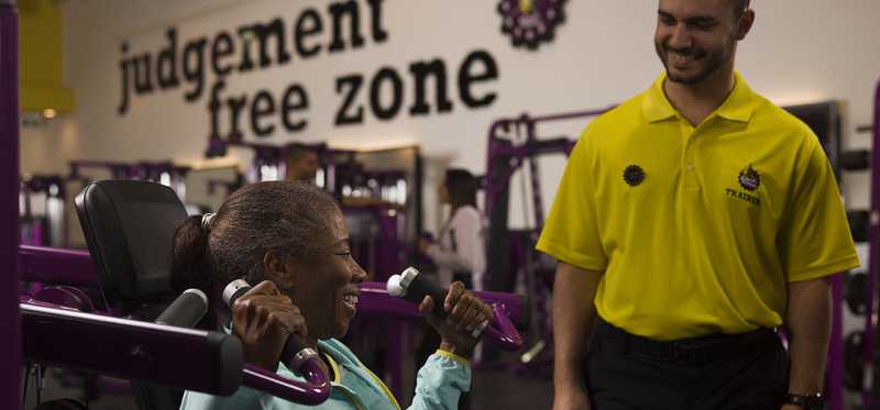 Planet Fitness employee assisting person on workout machine.