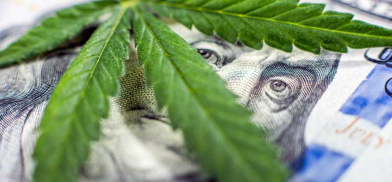 A pot leaf lays over Benjamin Franklin's face on a u.s. bill.
