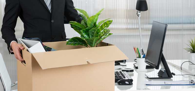 A person leaves an office with a box of belongings.