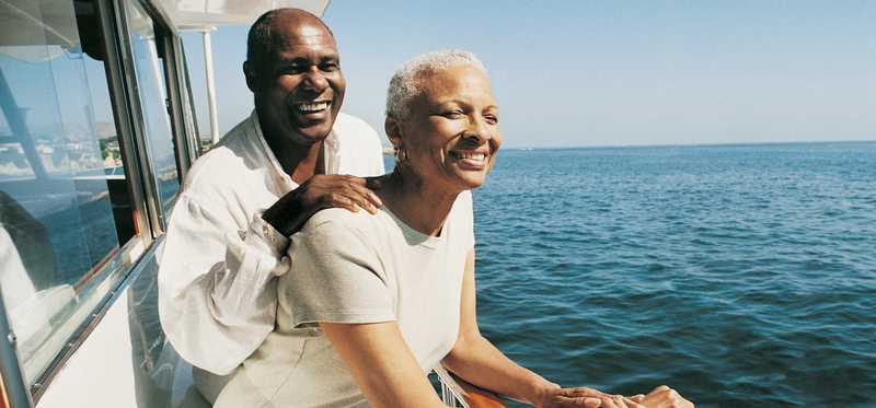 Two people smiling while standing on the side of a boat.