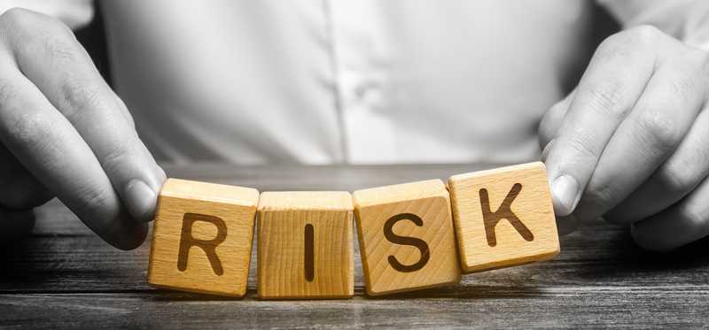 Person in white holding wooden blocks spelling Risk.