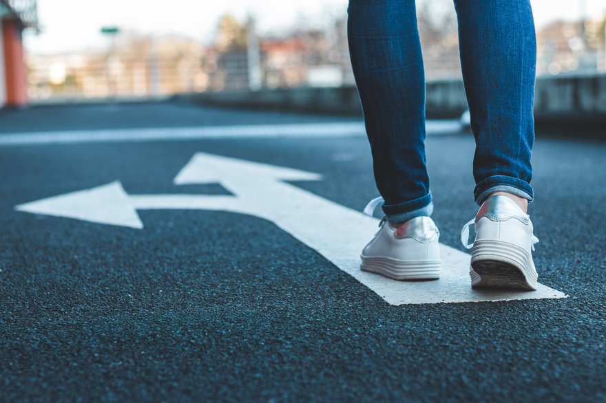 Pedestrian walking on road sign showing arrows pointing in different directions.