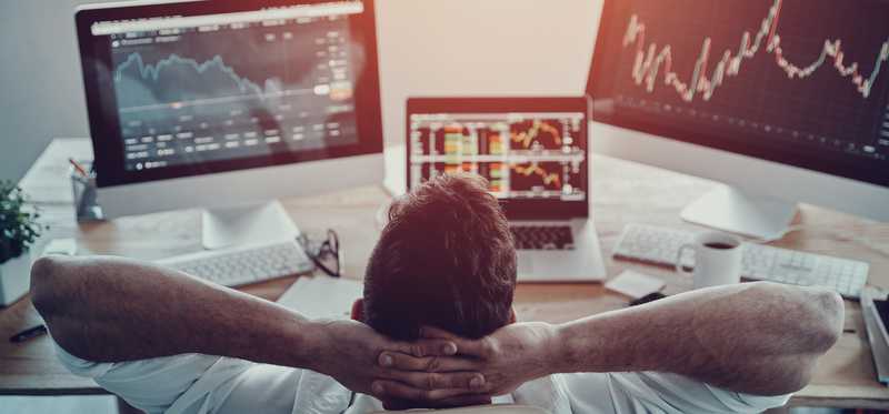 Satisfied investor leaning back while looking at multiple screens