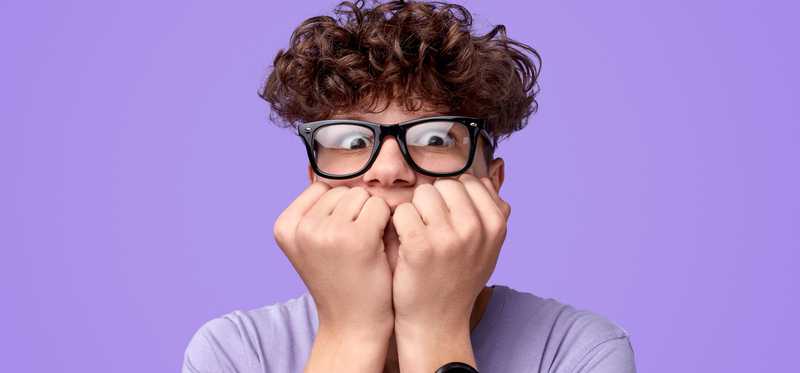 Nervous person with glasses and curly hair biting knuckles in fear.