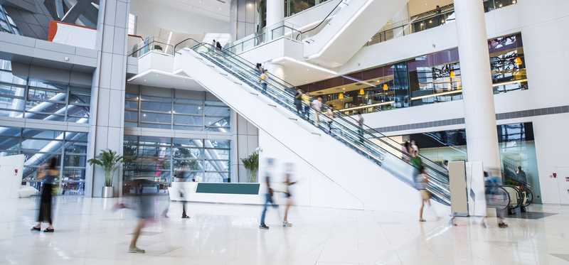 The inside of a modern shopping plaza with shoppers and escalator.