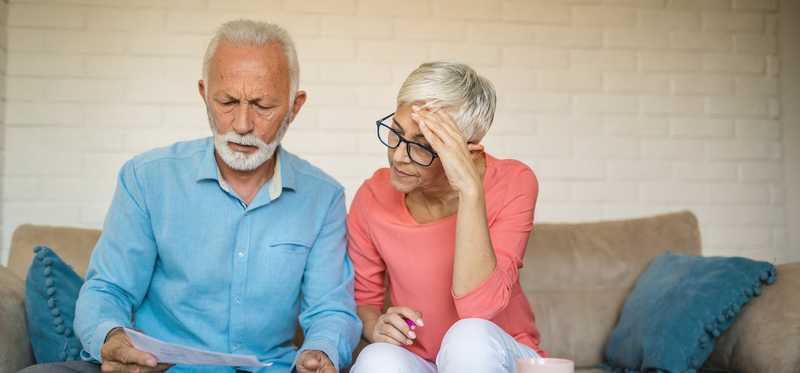 Two people sit on couch while looking at bills.