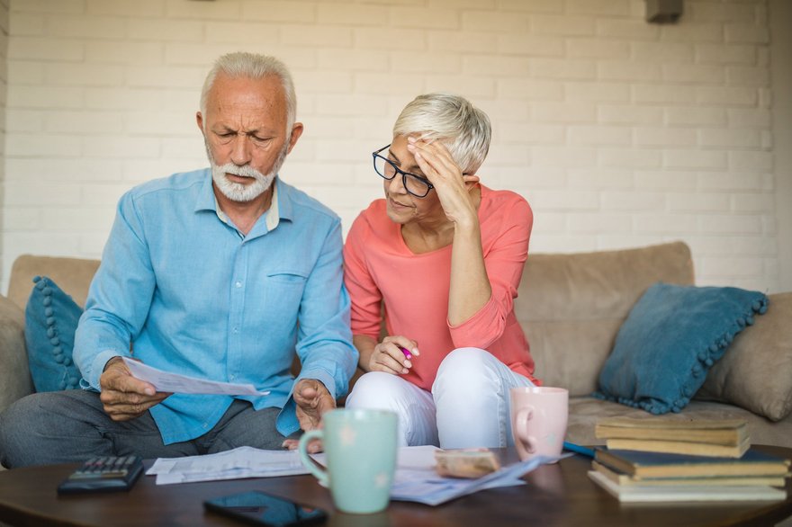 Two people sit on couch while looking at bills.