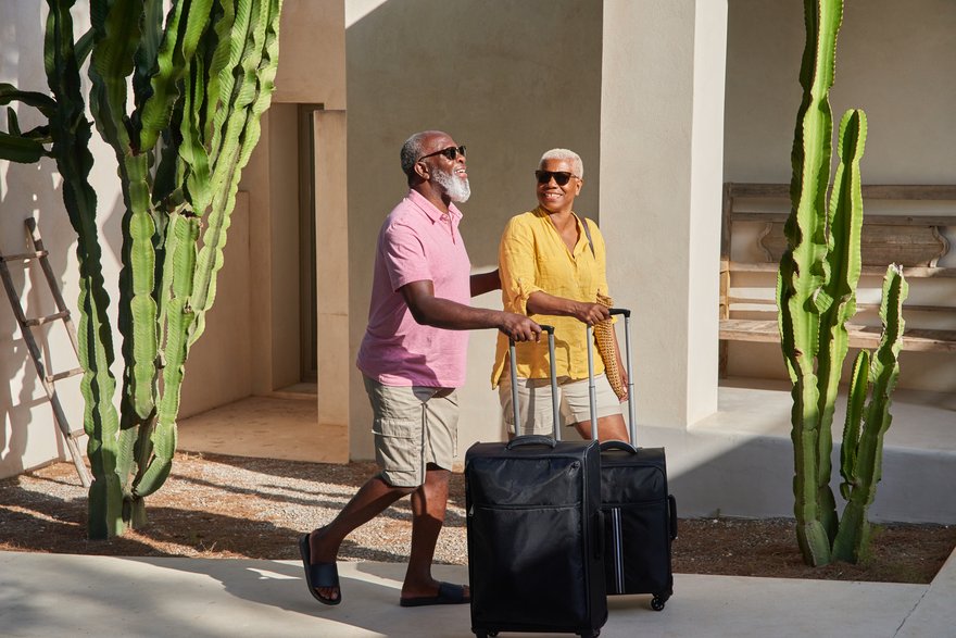 senior couple rolling suitcases down the street and smiling