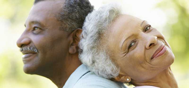 senior man and woman sitting back to back and smiling in park