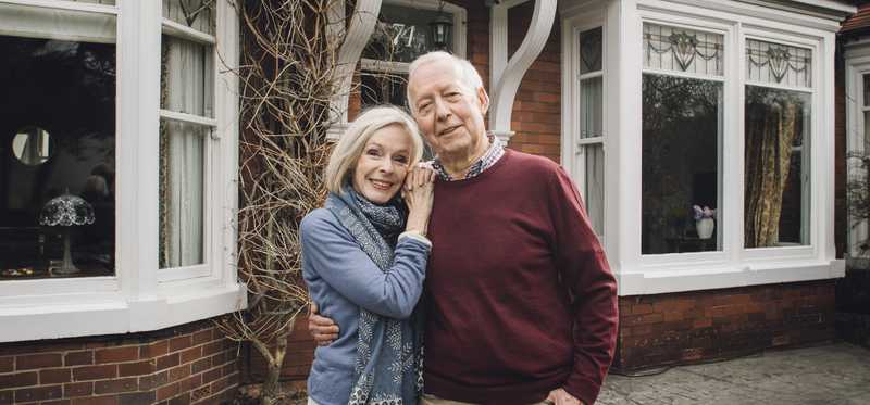 Two people smiling and holding each other in front of a house..