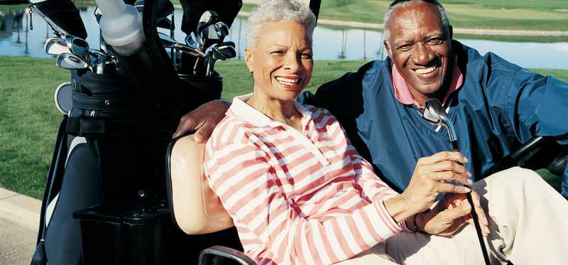 Two smiling people sit in golf cart.