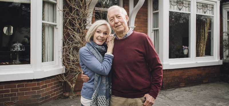 Two people smiling and holding each other in front of a house.