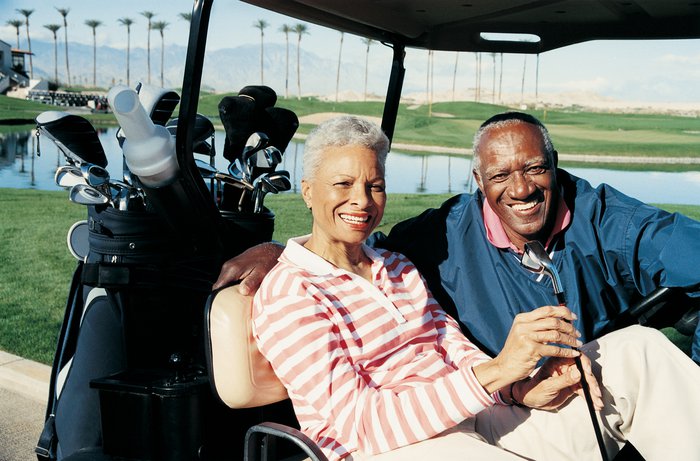 senior man and woman sitting in golf cart smiling