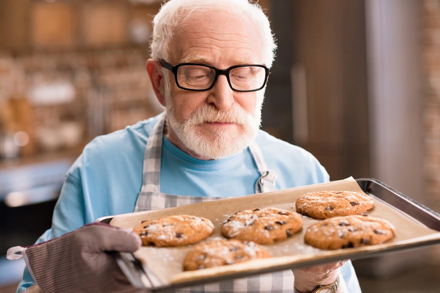 Senior in apron holding a tray of cookies.