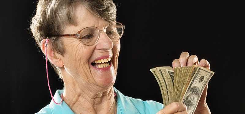 Person happily counting money against dark background.