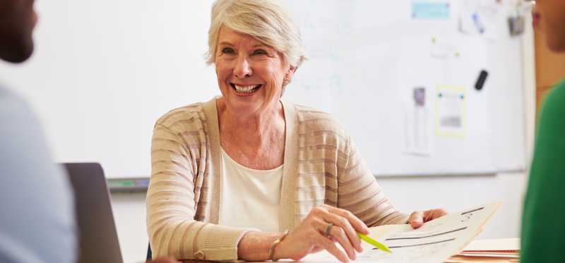Teacher in classroom talking to students and smiling.