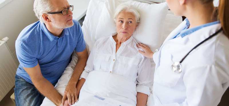 Older woman in bed with older man at one side and doctor at other side