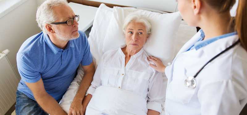 Doctor and visitor at bedside of patient.