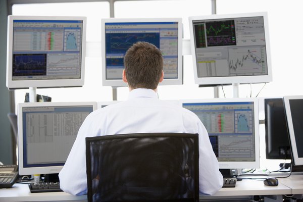 Investor sits in front of multiple screens showing investing charts and data.