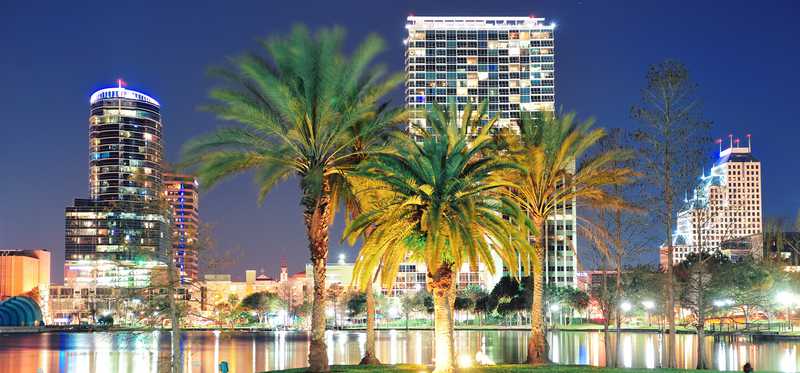 Skyline of downtown Orlando, Florida, at night with palm trees in background.