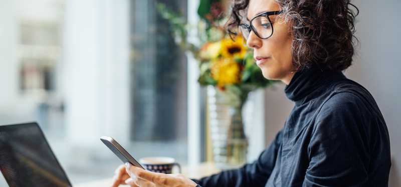 Person in glasses sitting at laptop and looking at phone.
