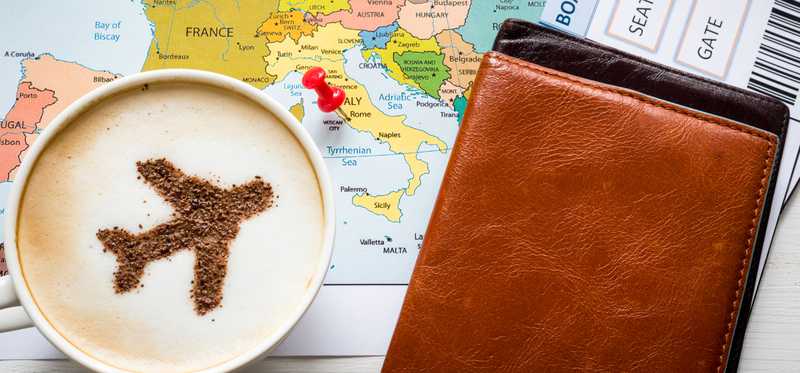 An airplane decoration made in the top of a latte alongside a map and travel tickets.