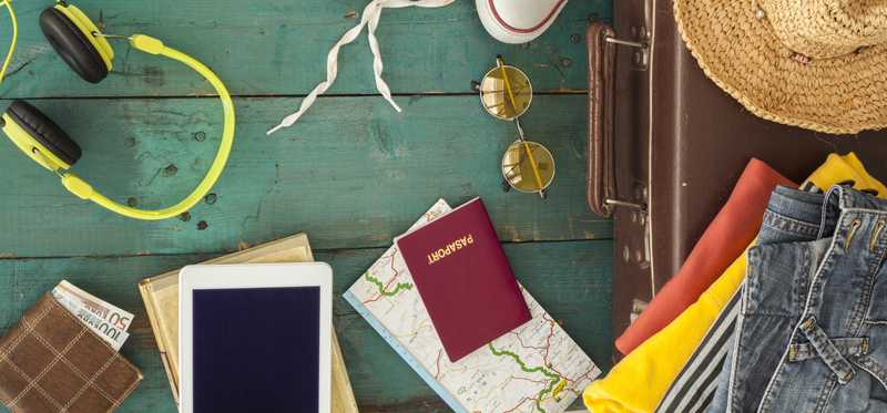A top-down view of items being packed for a trip: passport, camera, map, sunglasses, suitcase, and more.