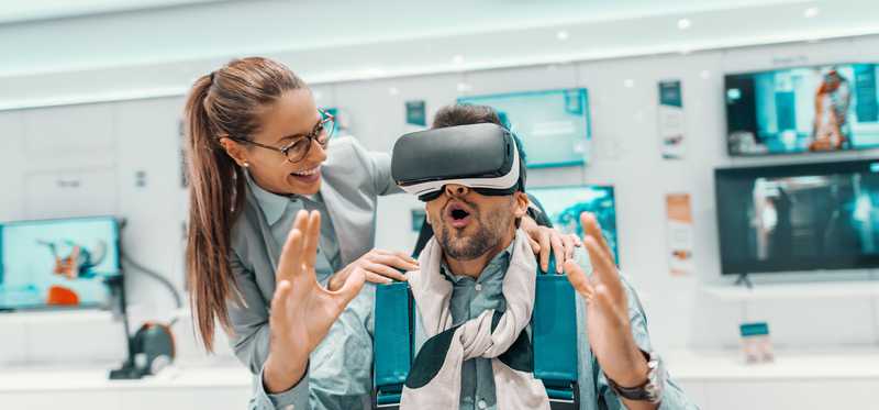 Worker assists person in trying on virtual reality headset.