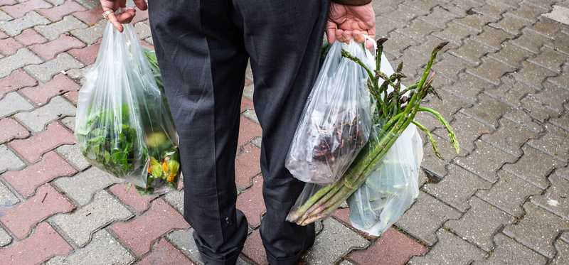 Man carrying produce including asparagus in clear plastic bags