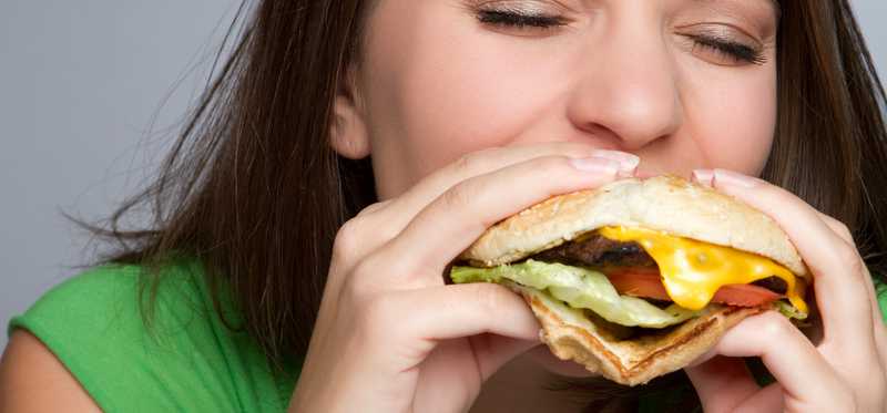 Woman bites into a cheeseburger.