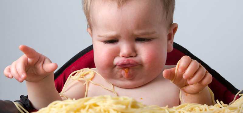 Baby in a high chair covered in spaghetti.