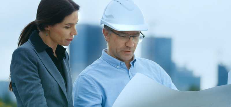 Woman talks to man in hardhat holding blueprint.