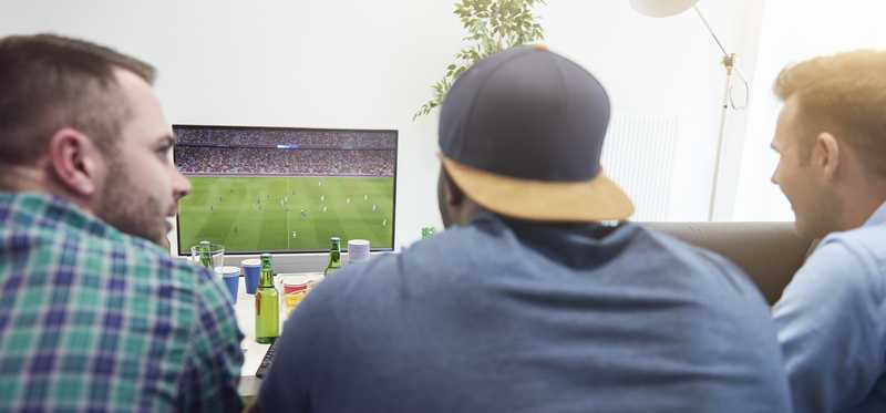 Three young men watch sports on a TV.