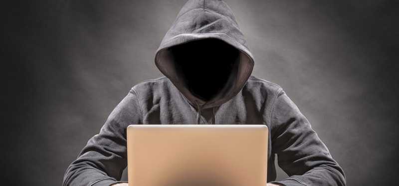 Hooded figure using a laptop.