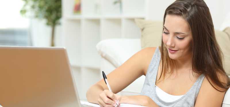 Young woman using a laptop and writing something down.