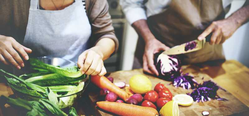 Two people in aprons chopping vegetables on a cutting board