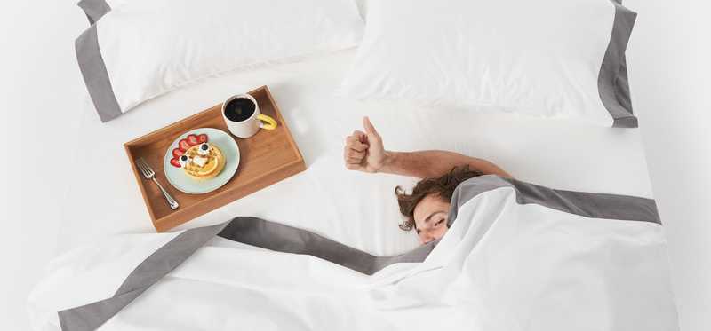 Person sleeping under covers on a mattress with a tray of breakfast beside them.