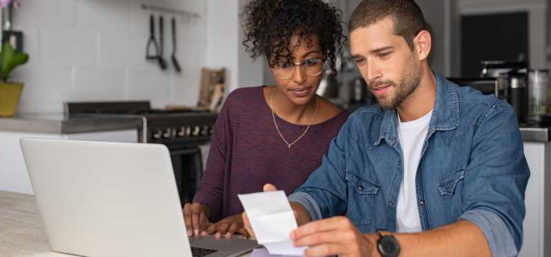 Two people looking at receipt and laptop in kitchen.