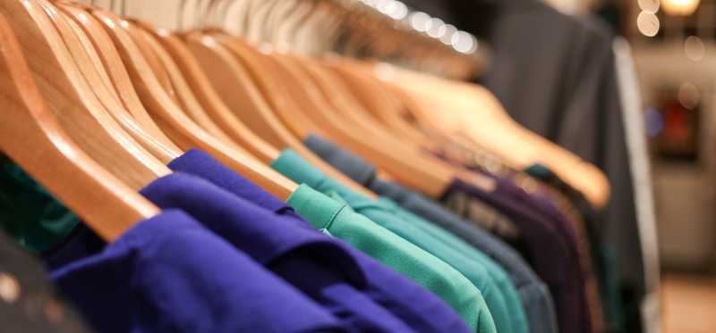 A rack of brightly colored tops on hangers.