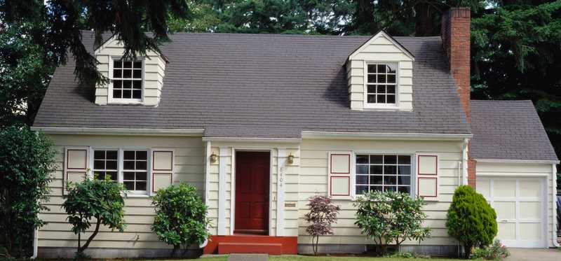 A white house with a red door in a suburban neighborhood.