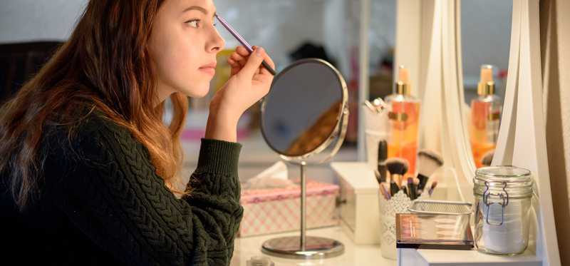 Woman does her make up in a mirror.